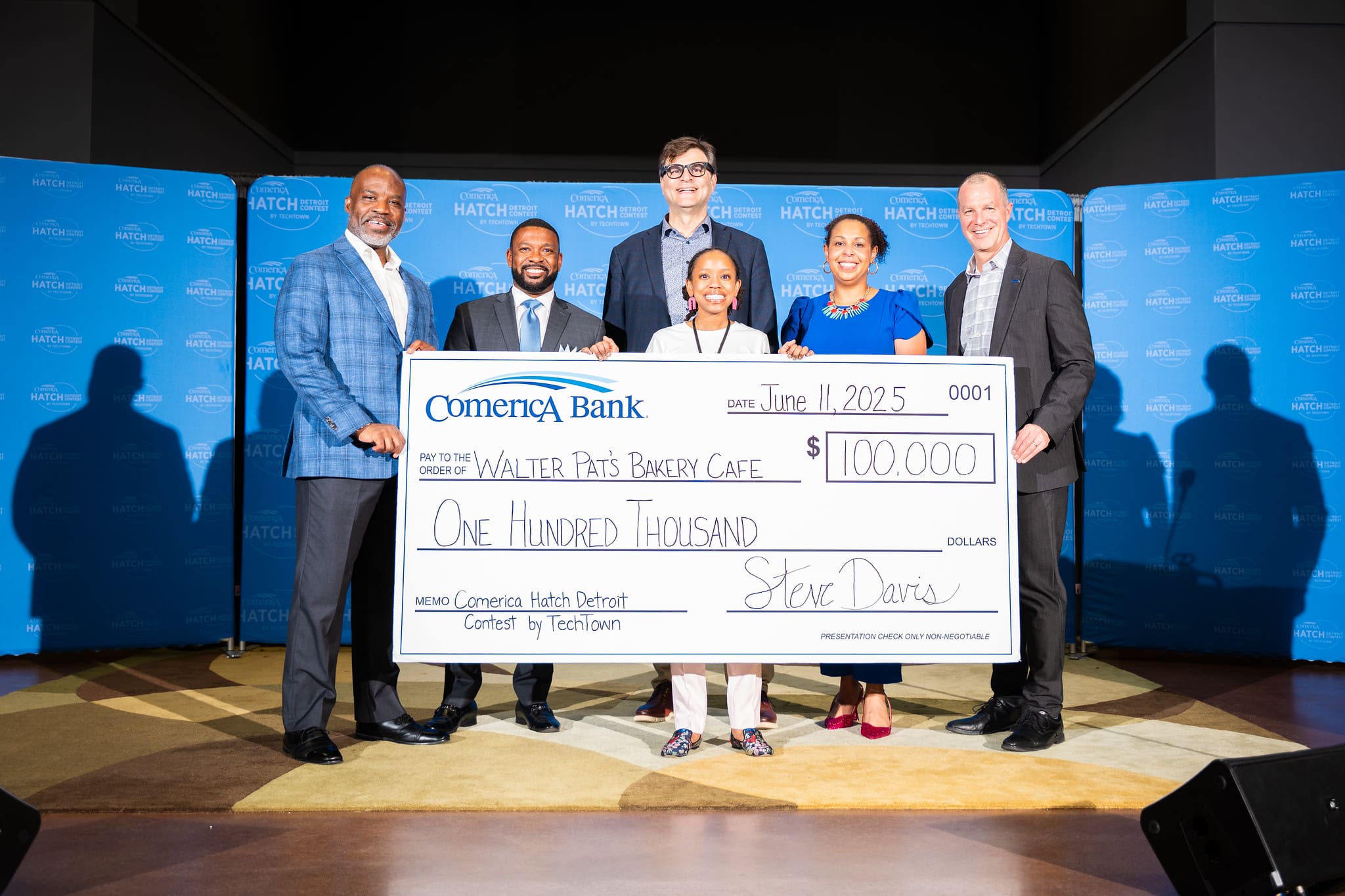 A winner of the TechTown Hatch Detroit competition, holding a big paper check made out to their company.