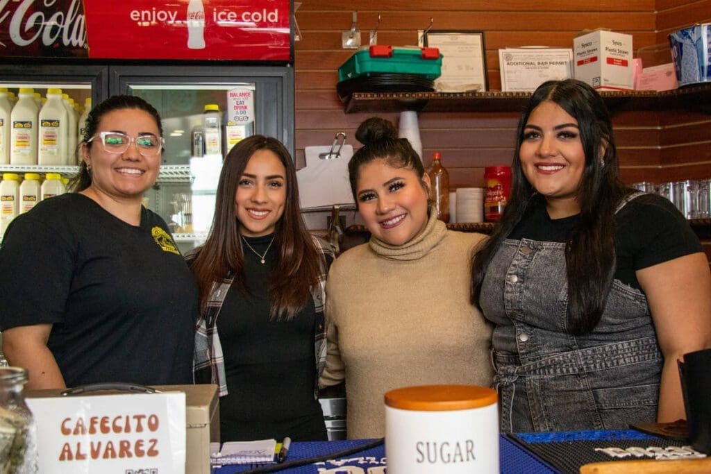 Four women stand behind a cash wrap while smiling and posing for a photo. 
