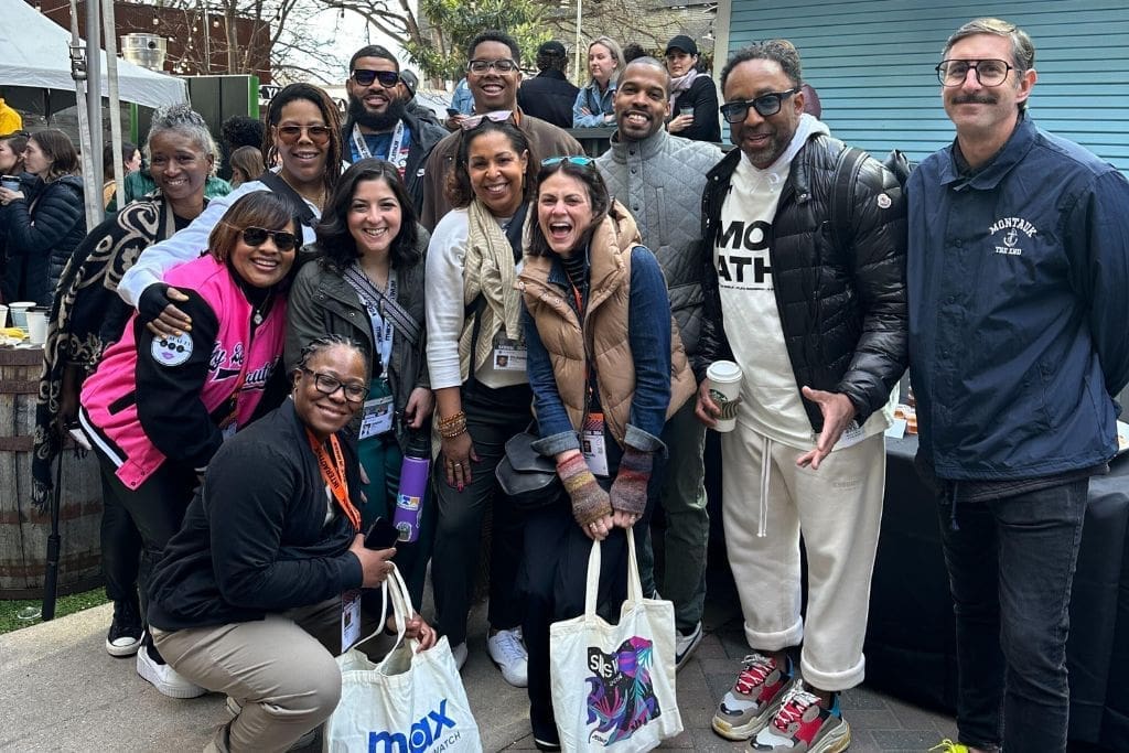 A group of people pose and smile for a photograph. They are outdoors at an event for by 2024 South by Southwest conference
