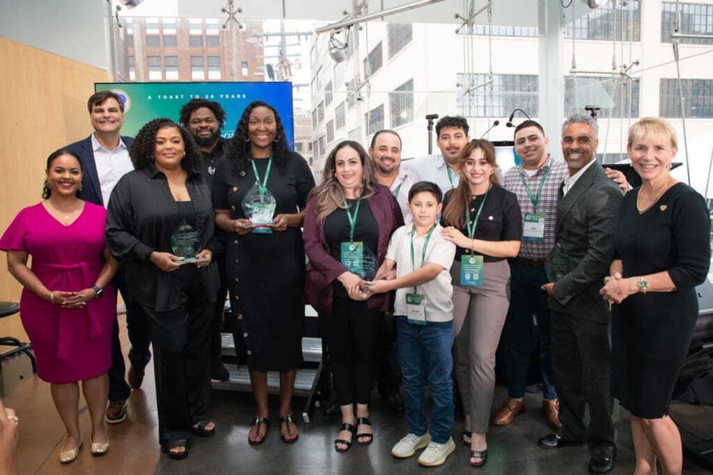 A group of people smiling for a photograph. Several of them are holding up Salute Award trophies from TechTown Detroit
