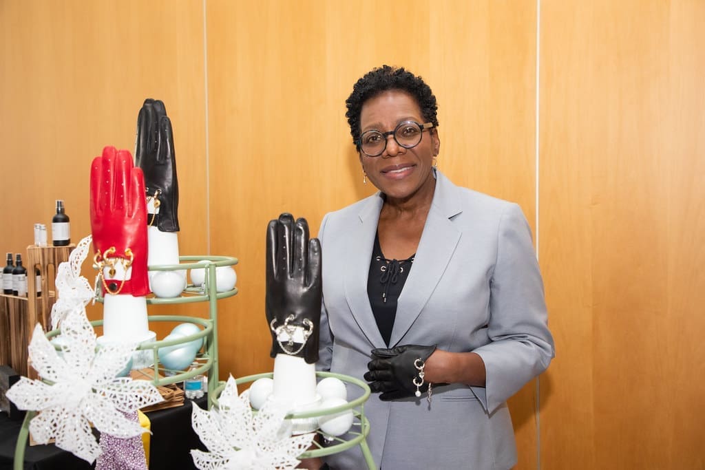 DaNita Weddle, founder of the The LuvGluv, smiles for a photo, standing beside a table display of leather gloves on hand mannequins